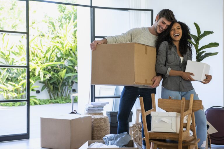 Happy couple carrying cardboard box and pot plant in new house