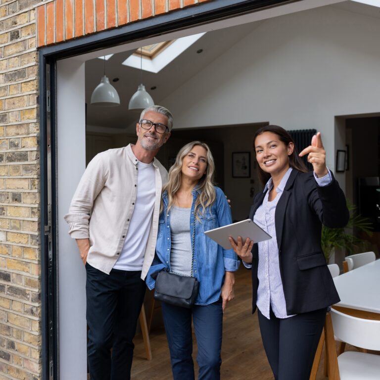 Real estate agent showing a house for sale to a couple and pointing outside - home ownership concepts