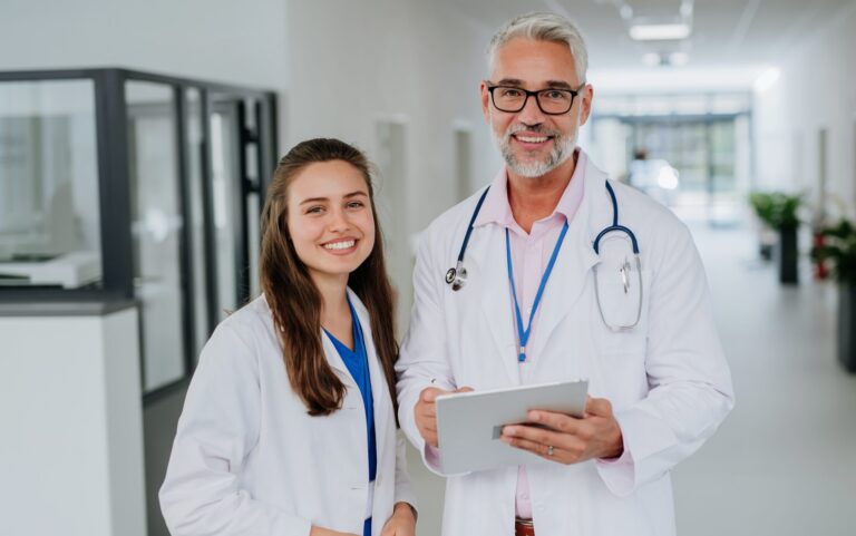 Portrait of elderly doctor with his younger colleague at a hospital corridor. Health care concept.