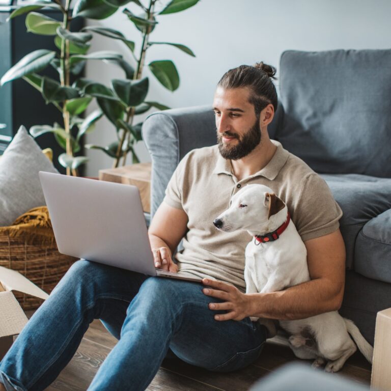 Young men moving in new house. He is happy and using laptop to organize everything. His pet dog is with him.