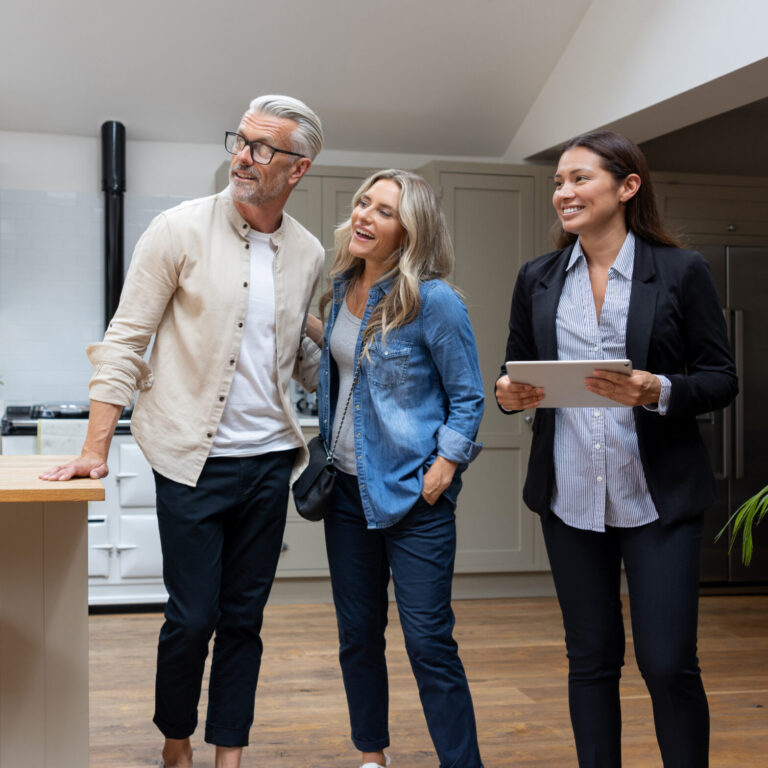 Real estate agent showing a house for sale to a couple and looking at the kitchen - home ownership concepts